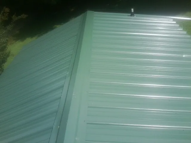 New green metal panels meeting at the ridge of a roof — Flat Roof Repair work by our crew in Levittown