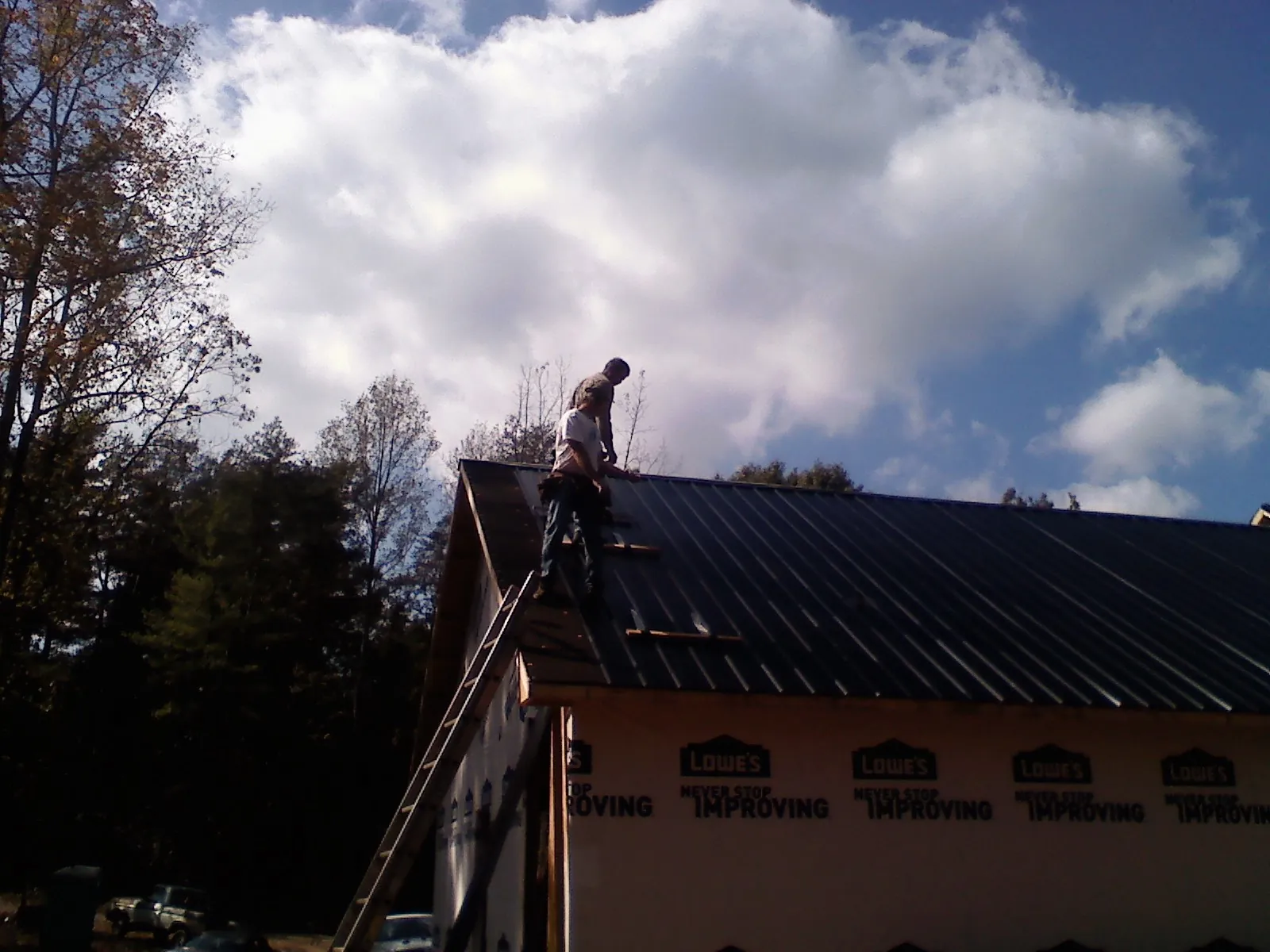 Roofer fastening dark metal panels high against a cloudy sky, from a Roof Inspection job in Levittown