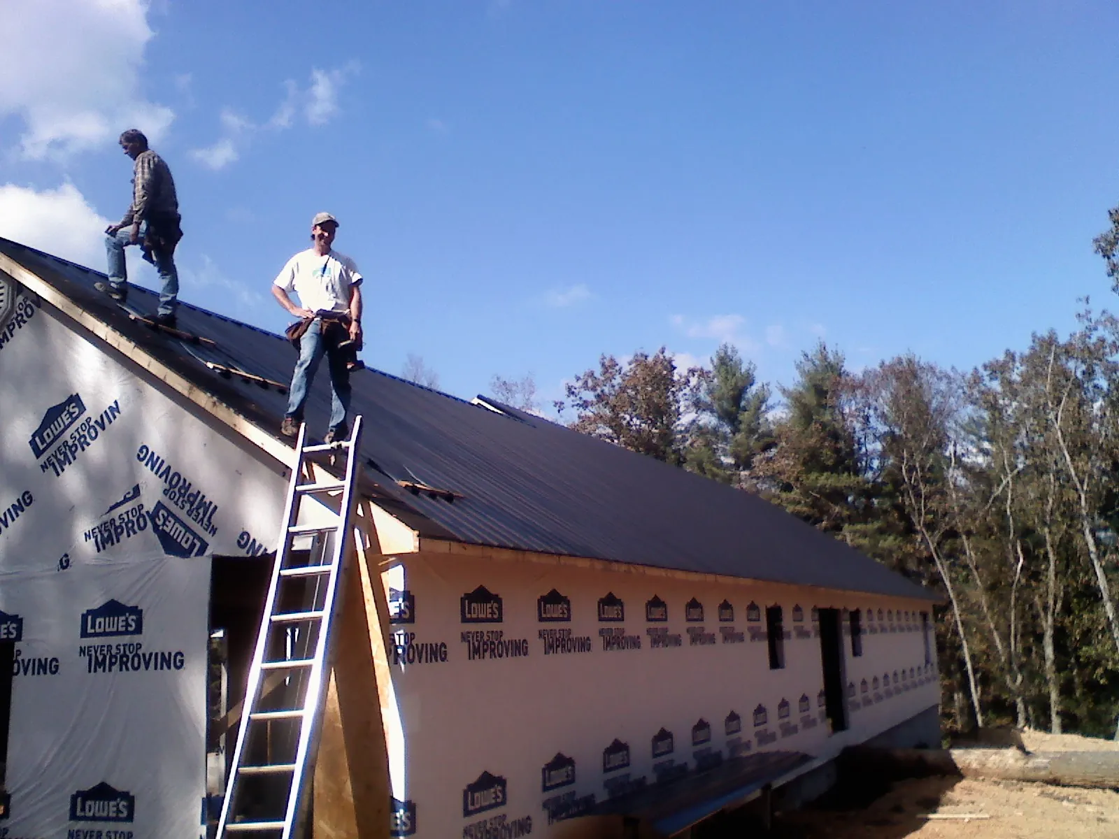 Two roofers standing on a long dark metal roof over a wrapped building in Levittown